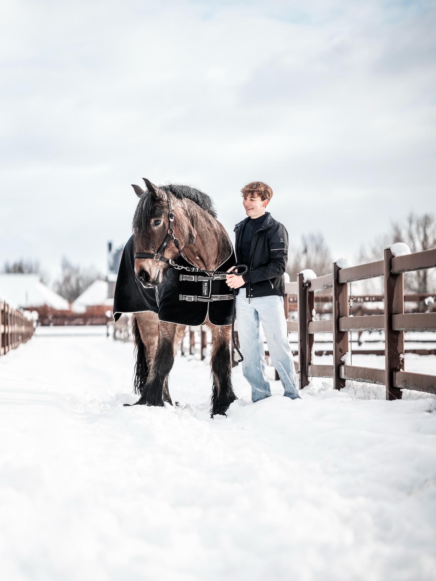 Robin lacht naast een trekpaard met deken in de sneeuw